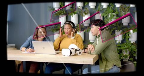 Team collaborating around laptop and vr headset in green coworking space, tech brainstorm