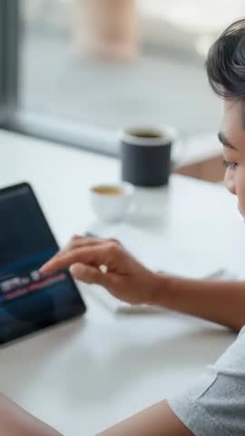 Vertical video of leaning Asian man tapping and swiping tablet while browsing at desk