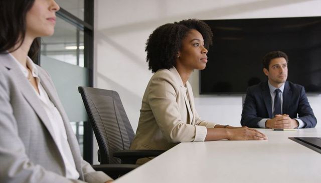 Focused businesswoman with curly hair listening in modern conference room meeting