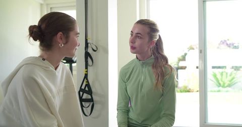 Female friends chatting in bright home gym wearing hoodie and athletic pullover