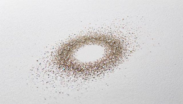 Forming iridescent gold glitter ring creating shimmering halo on white paper