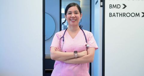 Confident nurse standing in clinic corridor wearing pink scrubs stethoscope and smartwatch