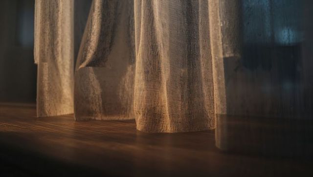 Glowing sheer curtains casting warm light and textured shadows across hardwood floor
