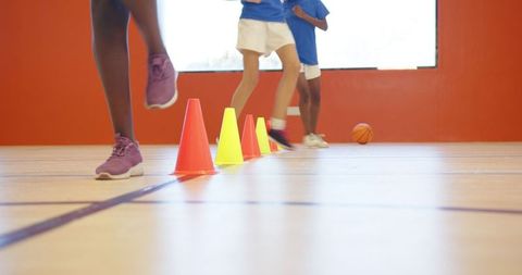 Girls practicing agility drills in gymnasium with orange cones