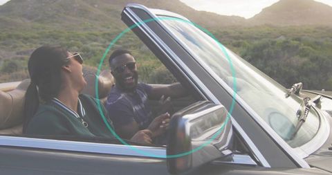 Couple laughing and driving convertible along countryside road during golden hour