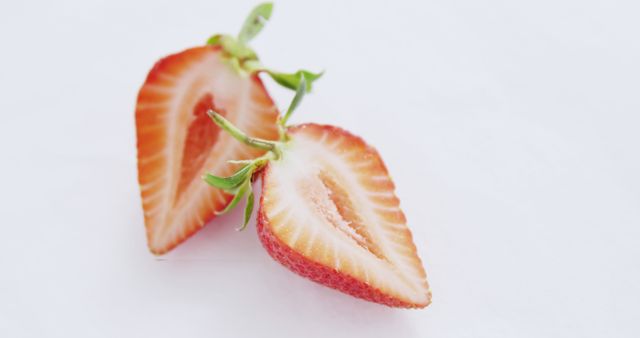 A fresh strawberry is sliced in half to reveal its juicy interior, with copy space. Its vibrant red color and fresh green leaves suggest ripeness and natural sweetness.