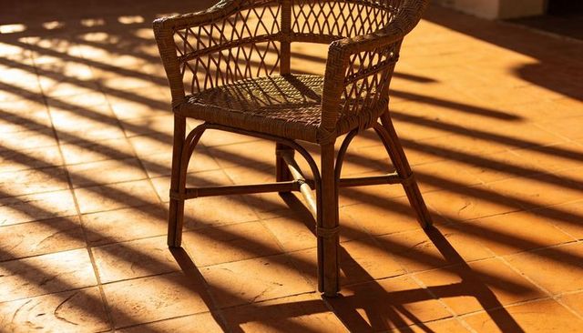 Wicker Rattan Armchair Casting Long Slatted Shadows on Sunlit Terracotta Terrace