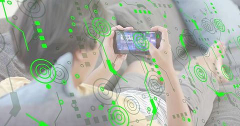 Asian man reclining on sofa playing mobile game with green ar hud overlay