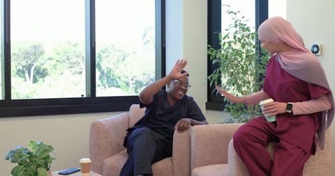 African american healthcare workers laughing and chatting in staff lounge on coffee break