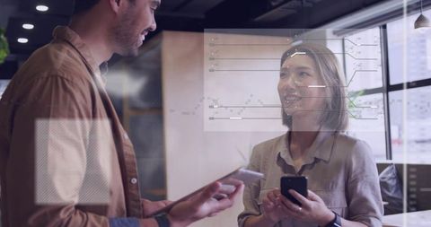 Coworkers collaborating and analyzing data on glass wall using smartphones and tablet