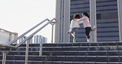 Urban Workout Duo Stretching Quads on Steps by Handrail in City Plaza Activewear Warmup
