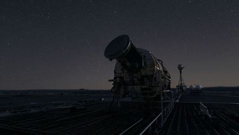 Large cylindrical telescope pointing upward under starry sky at remote observatory