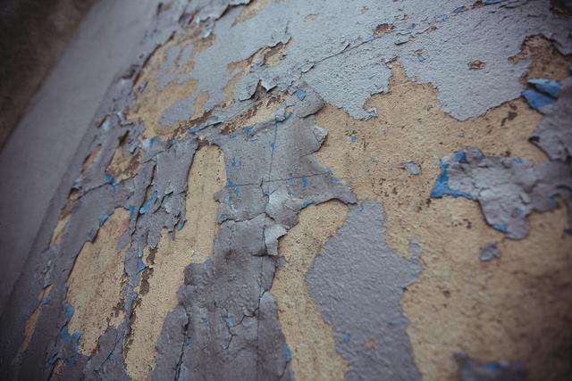 Close-up of an old wall with peeling paint, showcasing textures and signs of decay. Ideal for use in backgrounds, design projects, or as a texture overlay in graphic design. Suitable for themes related to urban decay, vintage aesthetics, or architectural details.