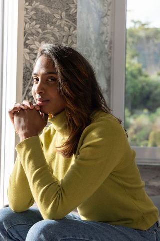 Young indian woman sitting by window contemplating, green turtleneck sweater portrait