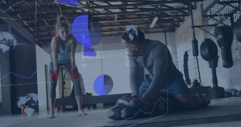 Coach adjusting heavy bag while boxer recovering in industrial gym with analytics overlay