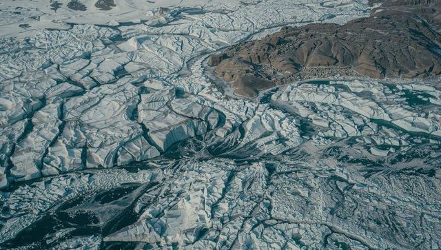Aerial view of fracturing polar pack ice flowing around barren rocky outcrop