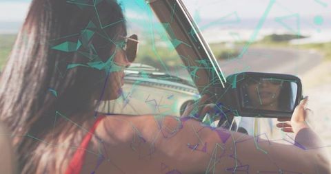 Driving woman adjusting rearview mirror on coastal road with teal geometric overlay