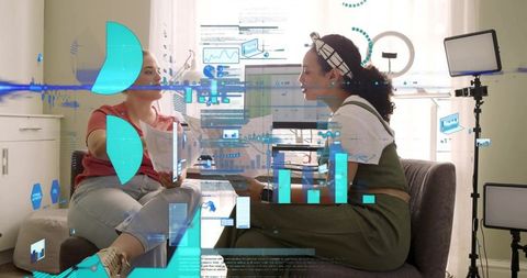 Two women discussing and reviewing holographic data visuals in modern living room studio