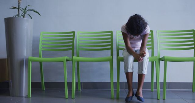 Young woman sitting on green chairs in a lobby, appearing sad and stressed. Can be used for concepts of mental health, waiting rooms, and patience.