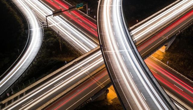 Curving highway overpass carrying white and red light trails at night aerial view