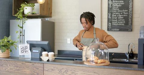 African american barista bagging pastry at modern coffee counter with qr code and takeaway cups