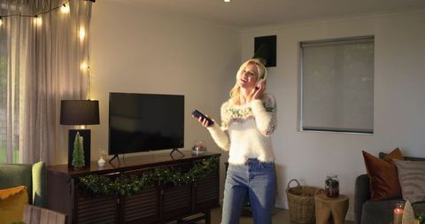 Woman enjoying music in cozy holiday living room wearing fuzzy sweater holding remote