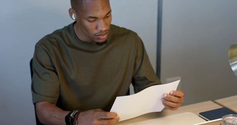 African American man reading document at minimalist home workspace with laptop and lamp