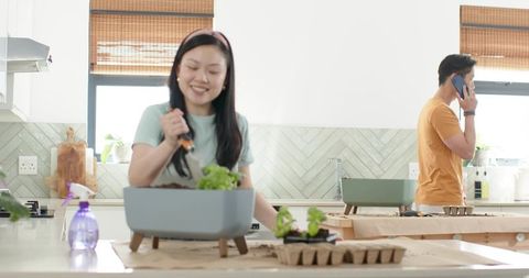 Asian couple tending tabletop herb garden in bright modern kitchen