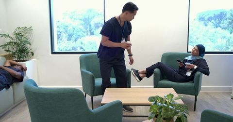 Healthcare staff relaxing in hospital breakroom enjoying coffee and smartphone on break