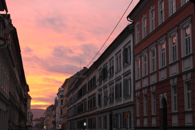 This captures a charming European street during sunset, featuring old buildings with classic architecture against a reddish sky. Ideal for travel articles, blogs about European cities, posters, or wall art art for a warm, nostalgic atmosphere.