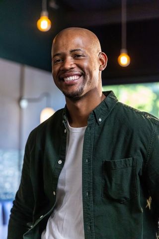 Smiling african american man wearing dark green shirt in cafe with warm pendant lights
