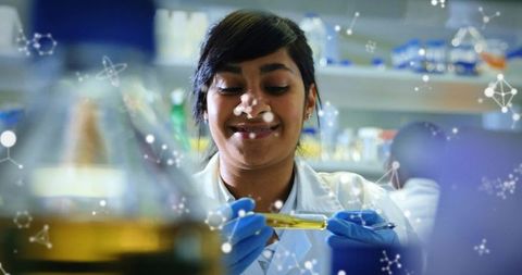 Female scientist examining yellow reagent vial at lab bench in lab coat and blue gloves