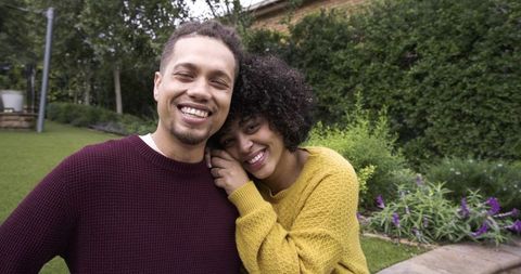African american couple smiling in garden showing engagement ring, cozy knit sweaters