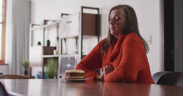 Sad woman in orange sweater sitting at wooden table with a cake conveys a sense of contemplation and melancholy. Suitable for themes of loneliness, reflection, mental health awareness, stories about mood and feelings.