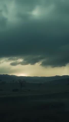 Vertical storm timelapse with shifting clouds over silhouetted hills and glowing horizon