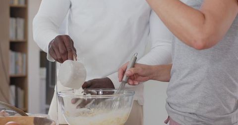 Couple pouring milk and whisking batter in bright kitchen preparing homemade baking
