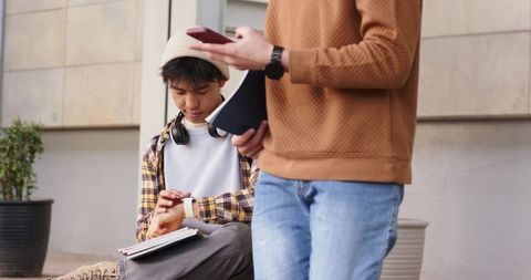 College friends checking smartwatch and taking notes on campus steps for study and teamwork