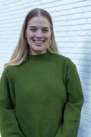 Smiling Blonde Woman Wearing Olive Green Sweater Outdoors by White Brick Wall