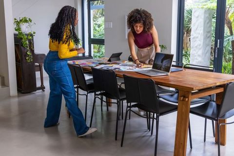 African american women collaborating on design planning with laptops and color swatches