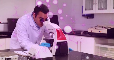 Male scientist examining sample through microscope in bright clinical laboratory