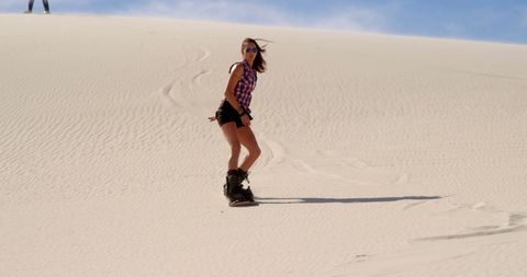 Woman Enjoying Sandboarding Adventure on Sunny Desert Dunes