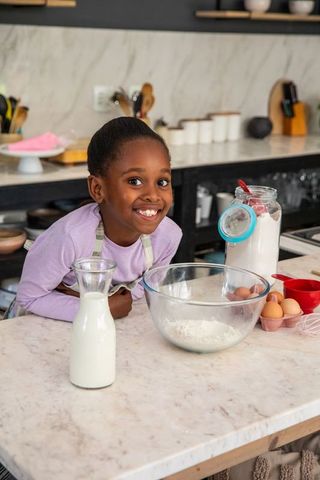African american girl smiling, baking on marble countertop with flour, milk and eggs