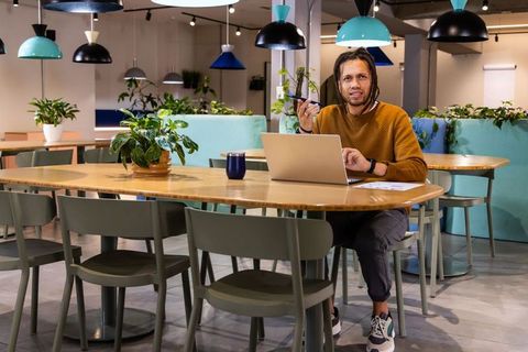 African american man working at coworking table with laptop, plants and pendant lights