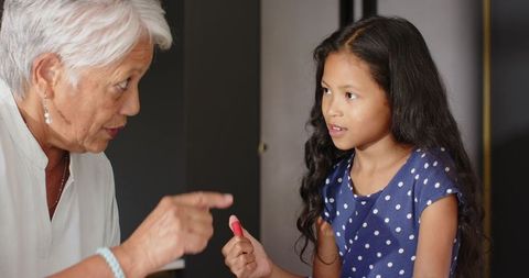 Asian grandmother pointing, granddaughter holding red crayon during learning moment