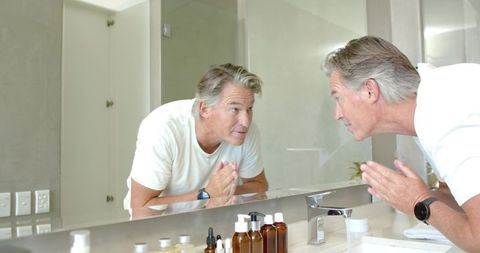Mature man checking facial skin in mirror during morning skincare and grooming routine