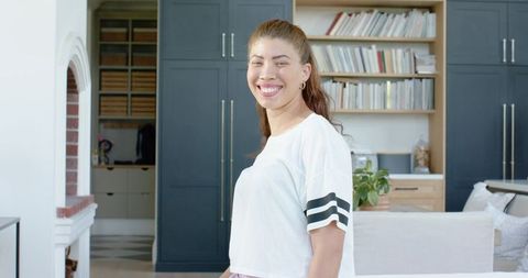 Smiling woman standing in modern home kitchen wearing casual white top with black stripes
