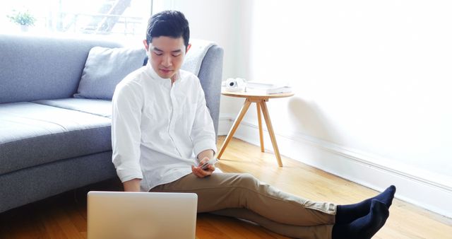 Young Man Using Laptop on Floor with Phone at Home - Download Free Stock Images Pikwizard.com