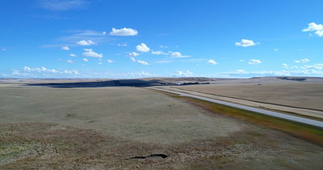 Wide view of an expansive prairie under a clear blue sky dotted with a few clouds. Perfect for backgrounds, landscape art, or projects focused on natural beauty, open spaces, and tranquility.