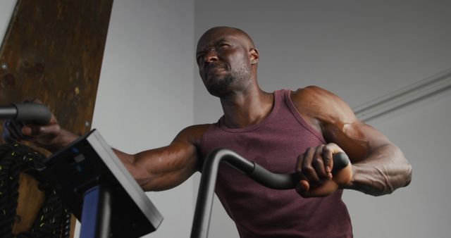 Muscular athlete working out intensely on an exercise bike, showcasing determination and strength. Suitable for fitness, health, and exercise-related materials. Can be used in advertisements, magazines, blogs, and social media posts promoting a healthy lifestyle and fitness workouts.