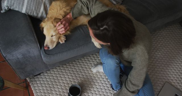 Woman gently petting sleeping dog on couch with hot coffee nearby. Perfect for concepts of home relaxation, pet bonding, and cozy moments. Can be used in articles or websites related to pet care, home comfort, and lifestyle.